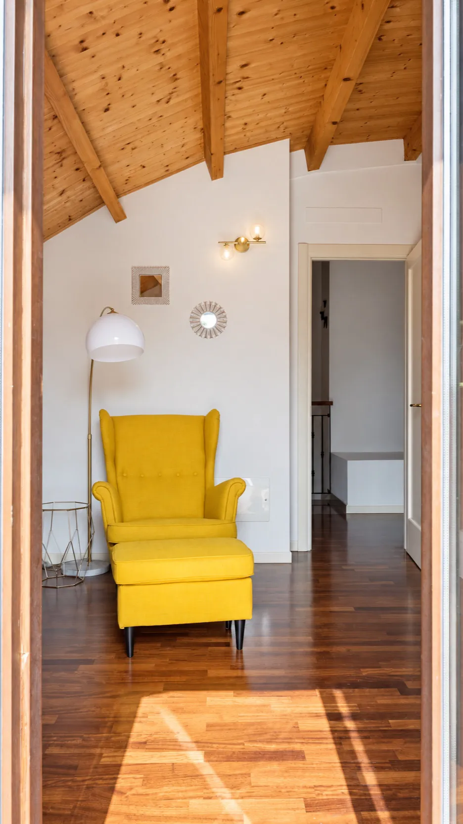 Scorcio dello studio: la poltrona gialla sotto il soffitto in legno, la porta verso il disimpegno